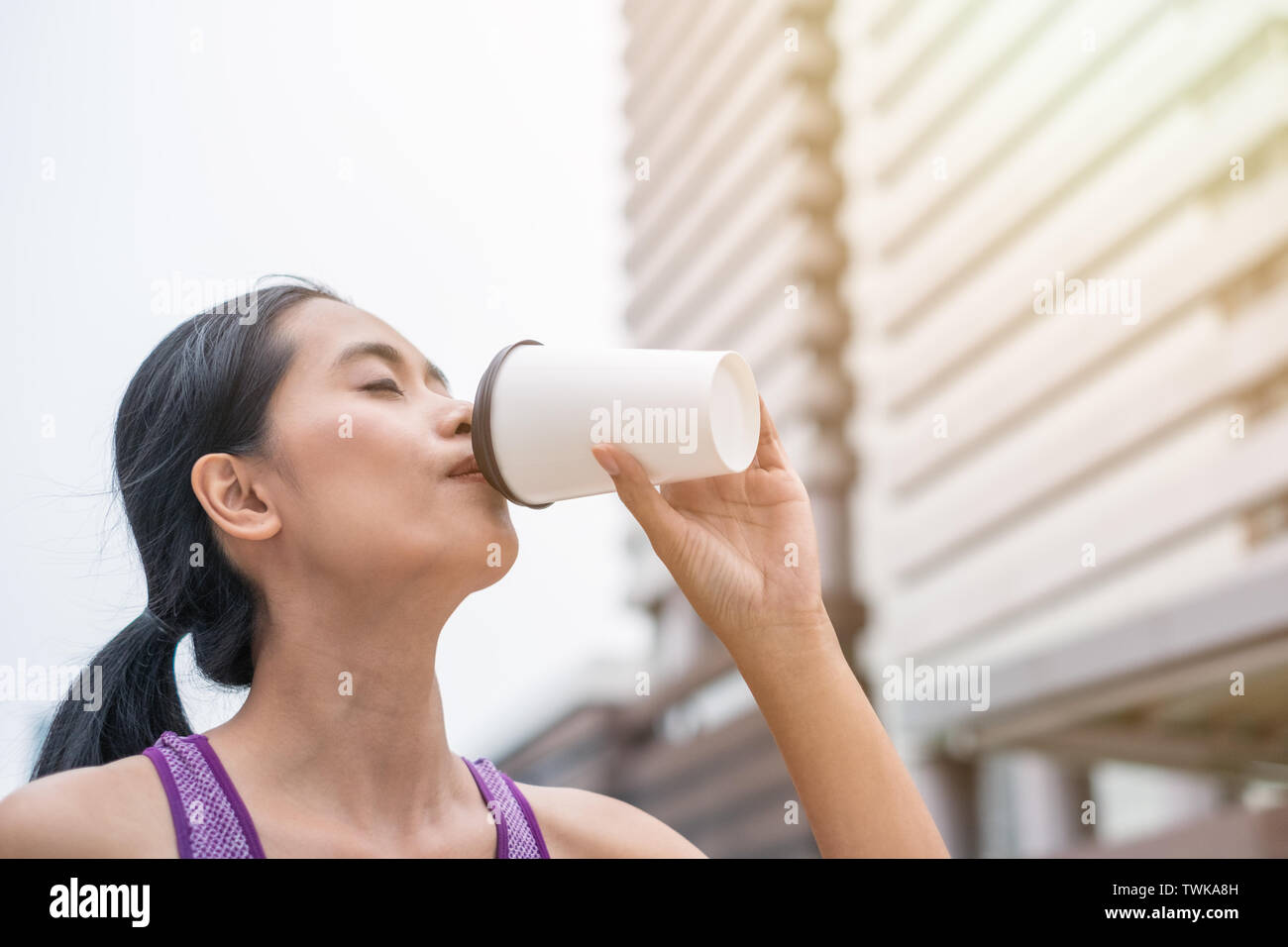 Tan woman drinking coffee after exercise is completed at urban Stock