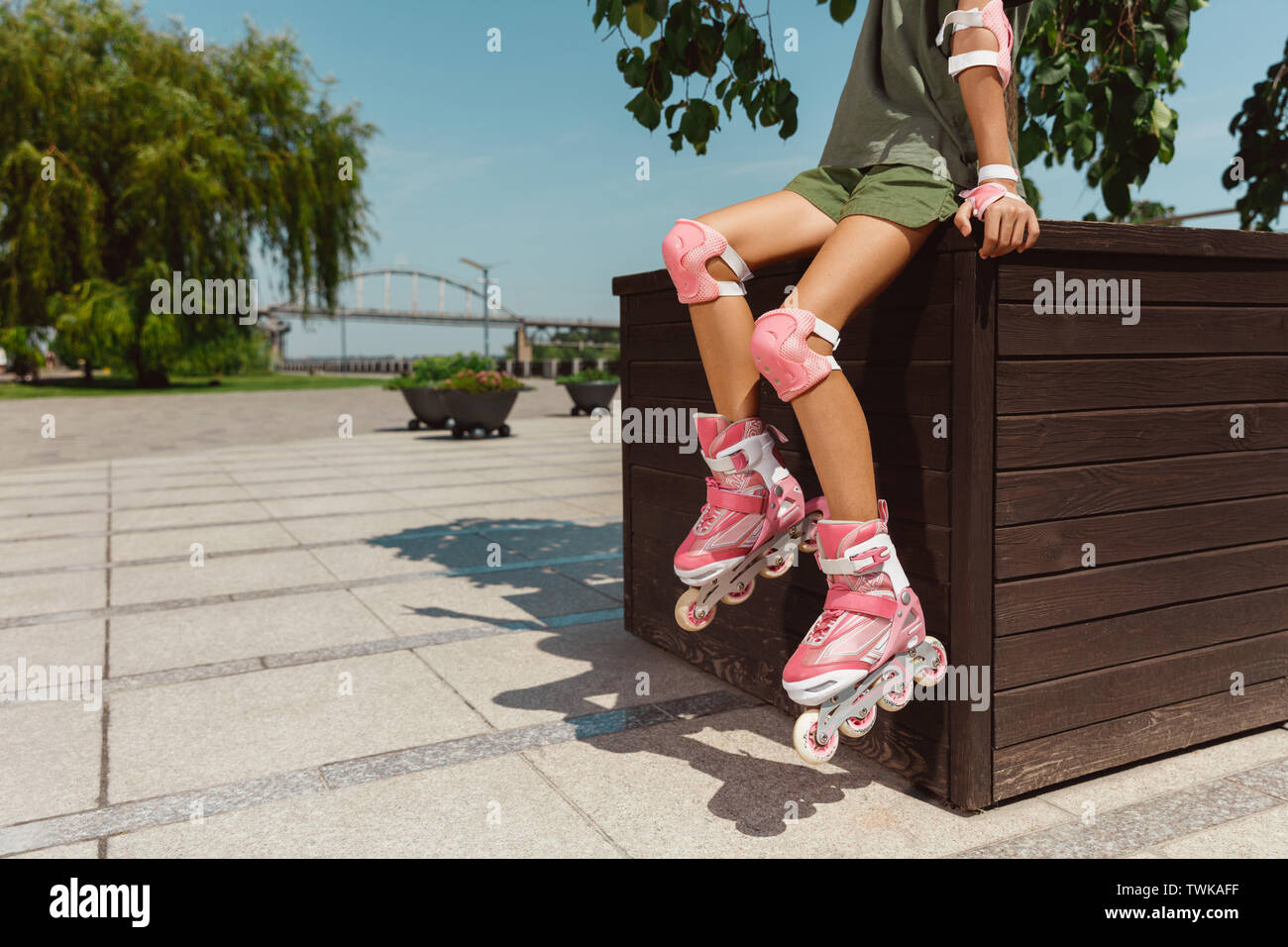 Teenage girl in a helmet learns to ride on roller skates holding a balance or rollerblading and spin at the city's street in sunny summer day. Healthy lifestyle, childhood, hobby, leisure activity. Stock Photo