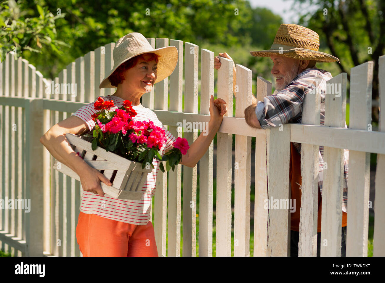 Speaking with neighbor. Redhaired aged woman holding pink flowers