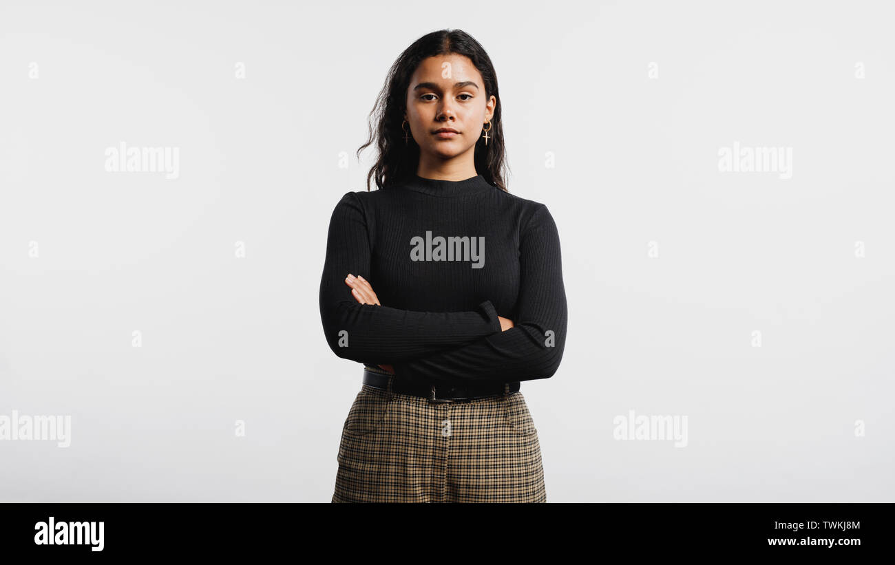 Portrait of young woman looking at camera. Woman standing against white background with her arms crossed. Stock Photo