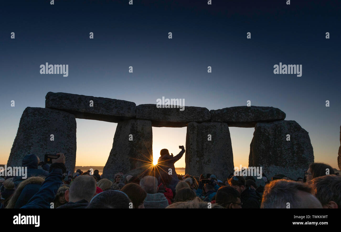 Visitors to Stonehenge in Wiltshire raise their mobile phones to capture the moment as they witness the perfect sunrise behind the ancient monument on Stock Photo
