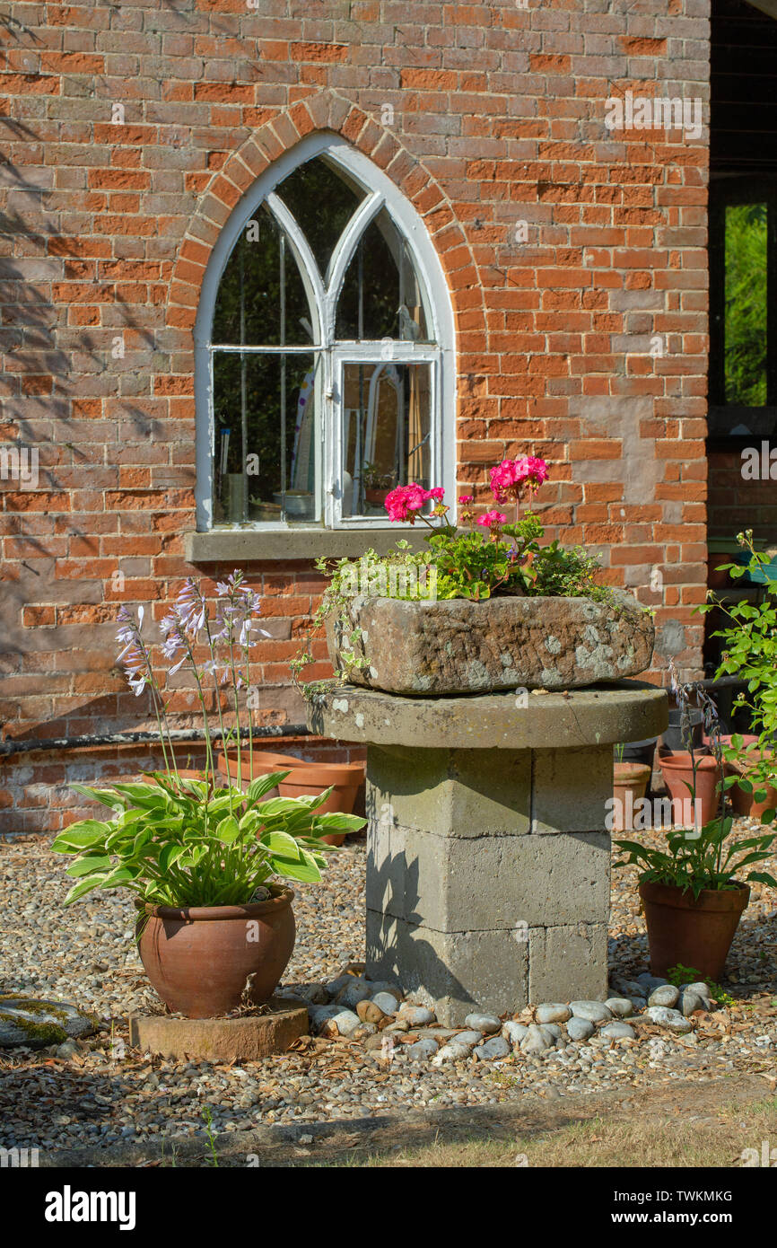 Stone trough. Mounted on a breeze block plinth and a mill stone. Now used as a plant container garden ornament. Raised above ground level to frustrate rabbits, and reduce slug and snail damage to sensitive cultivated plantings. Stock Photo