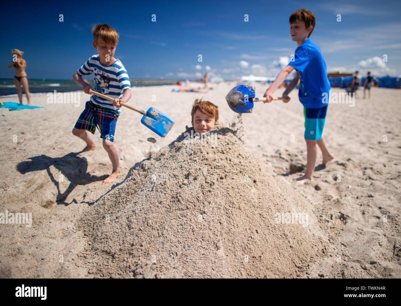 Rostock, Germany. 21st June, 2019. Tilman from Falkensee near Berlin is dug  into the sand by his brothers Bennet and Frieder on the beach of  Warnemünde. Summer temperatures and sunshine lure locals