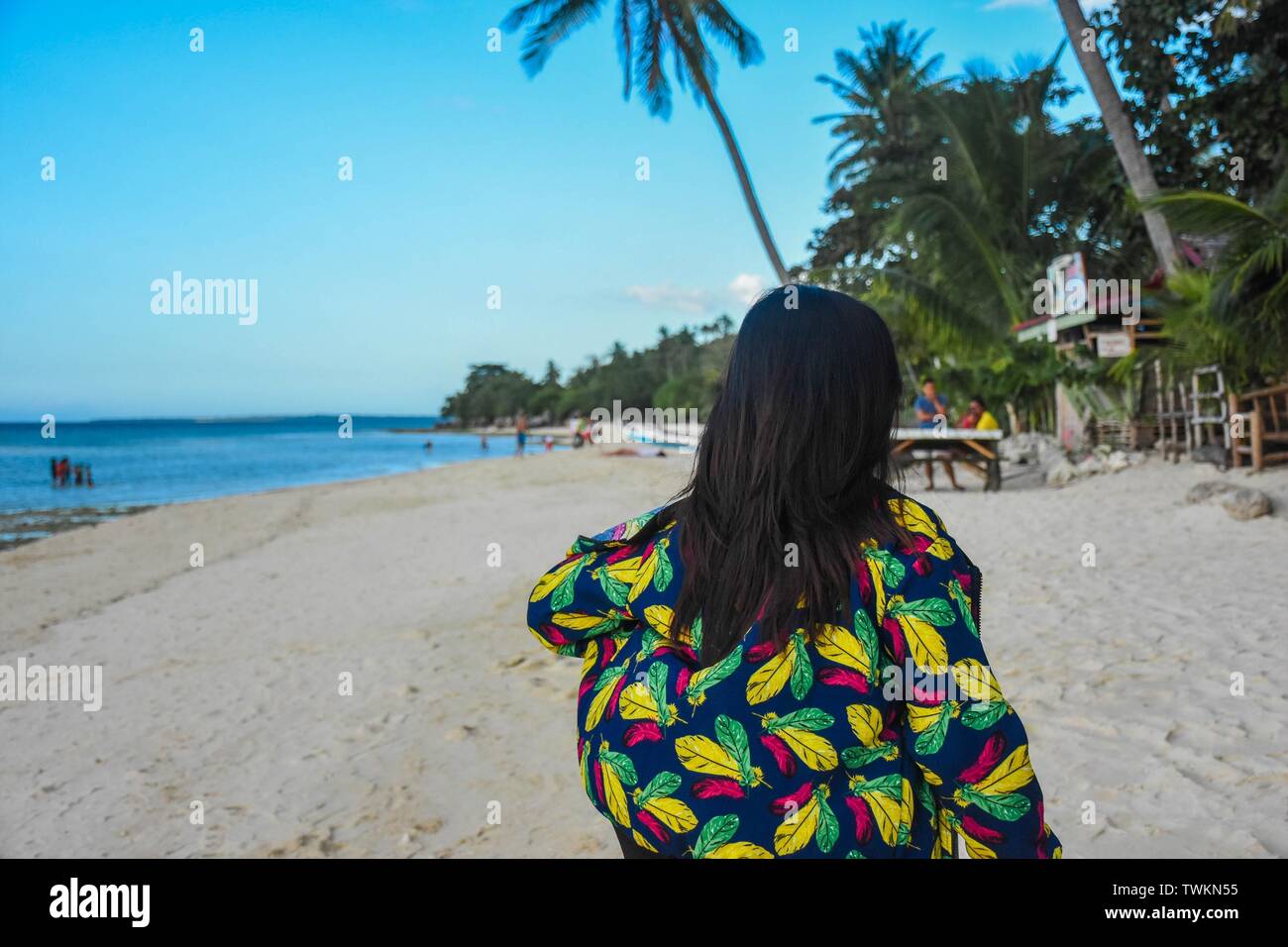 Female in a coat with colorful feathers walking on a populated beach ...