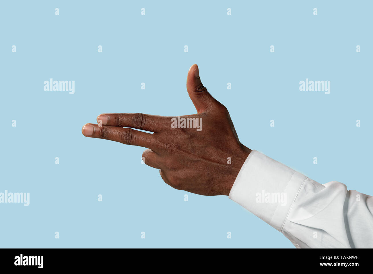 Male hand in white shirt demonstrating a gesture of gun, handgun or pistol  isolated on blue studio background. Concept of business, office, work.  Negative space to insert your text or image Stock