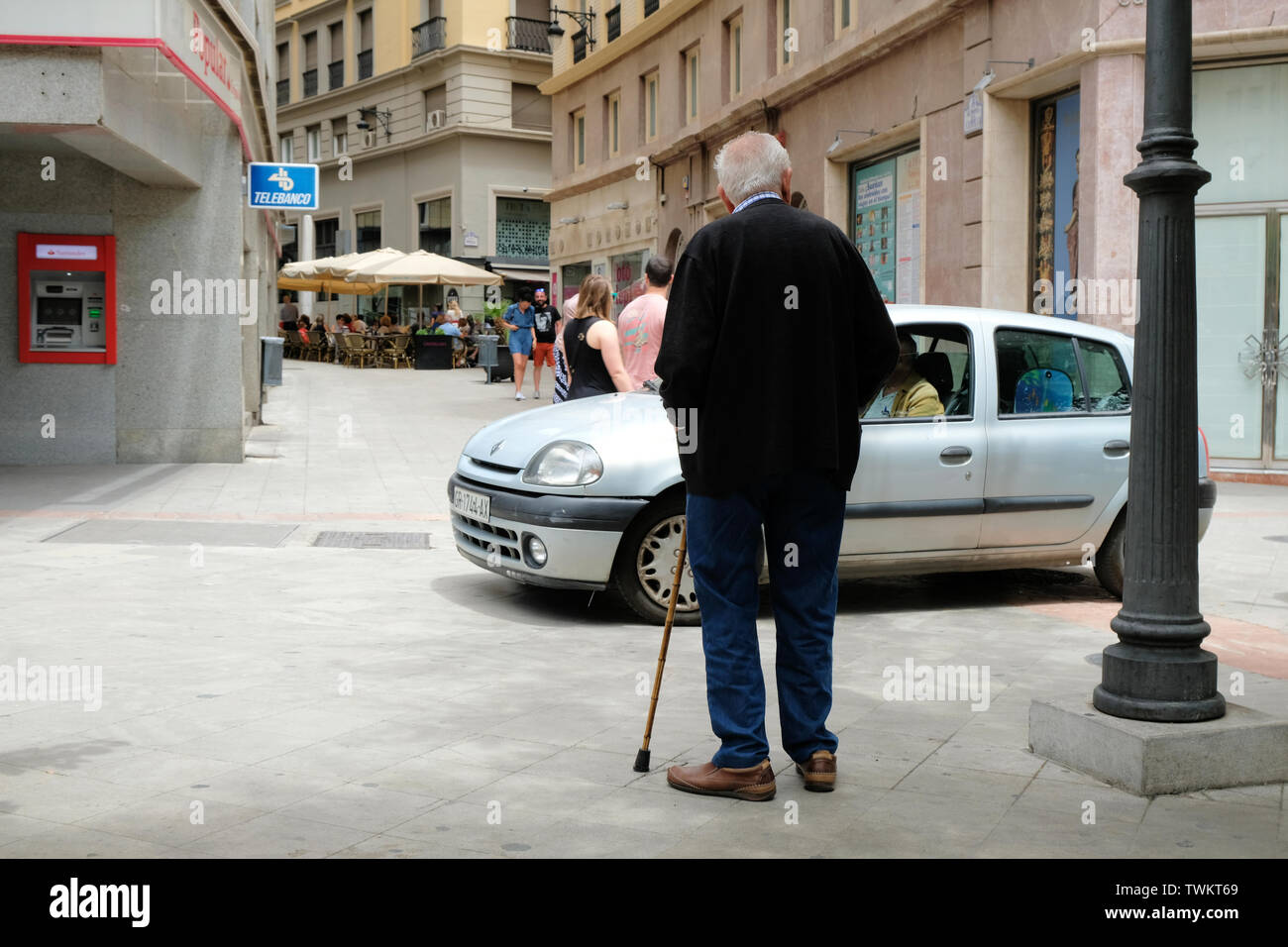 Old gray haired man with a cane stopping to let a car before crossing the street in Granada, Spain. Stock Photo
