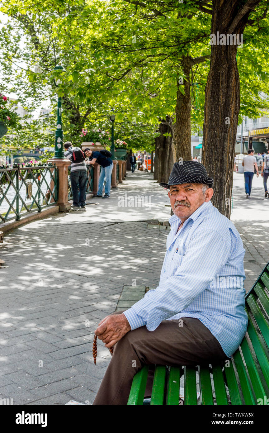Eskisehir, Turkey - May 16, 2015: Elderly man dressed in black hat, blue shirt and brown pants sitting on a bench in the city center. Stock Photo