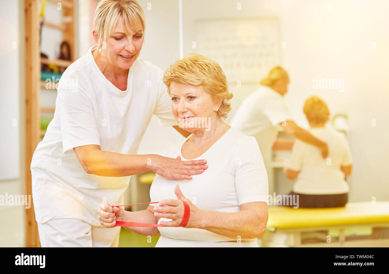 Senior with Theraband at physiotherapy makes strength training for postural correction Stock Photo