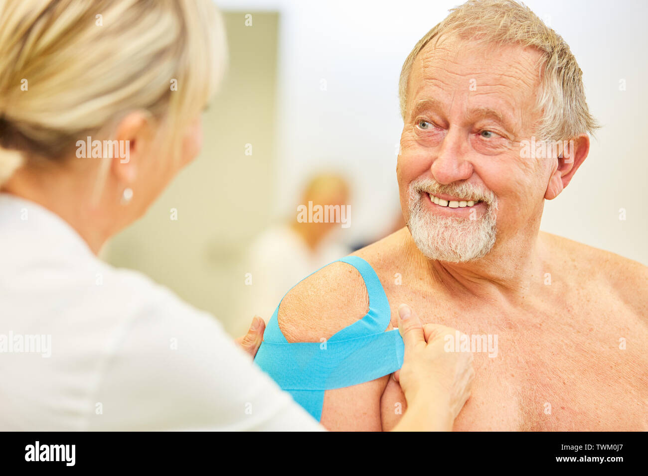 Senior patient is pleased about Kinesio taping on his shoulder in the physiotherapy Stock Photo
