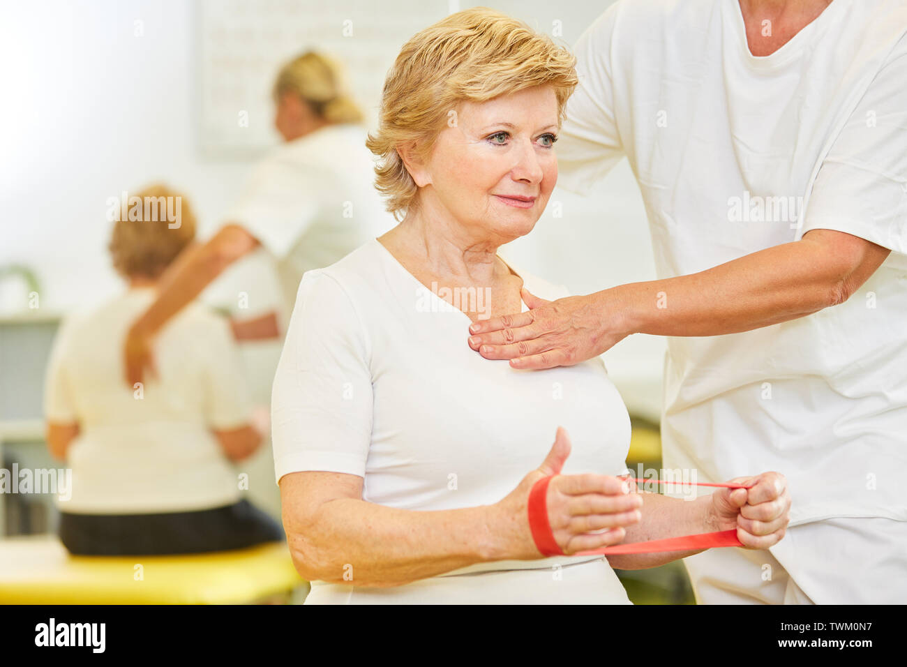 Senior as a patient makes exercise with the latex band against back pain in physiotherapy Stock Photo