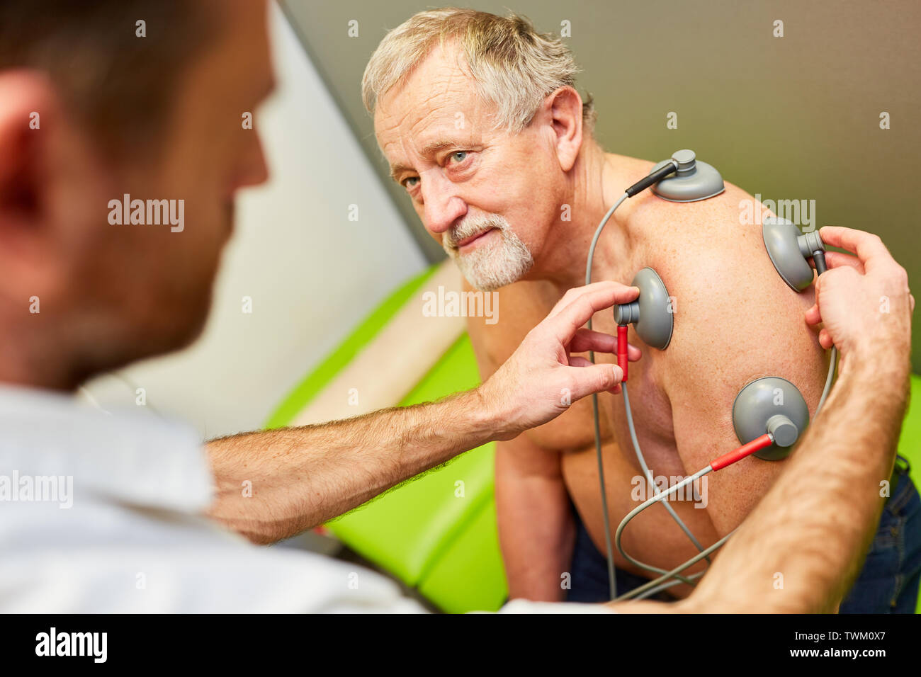 Orthopedist makes stimulation current therapy with senior patient and attached vacuum electrodes Stock Photo
