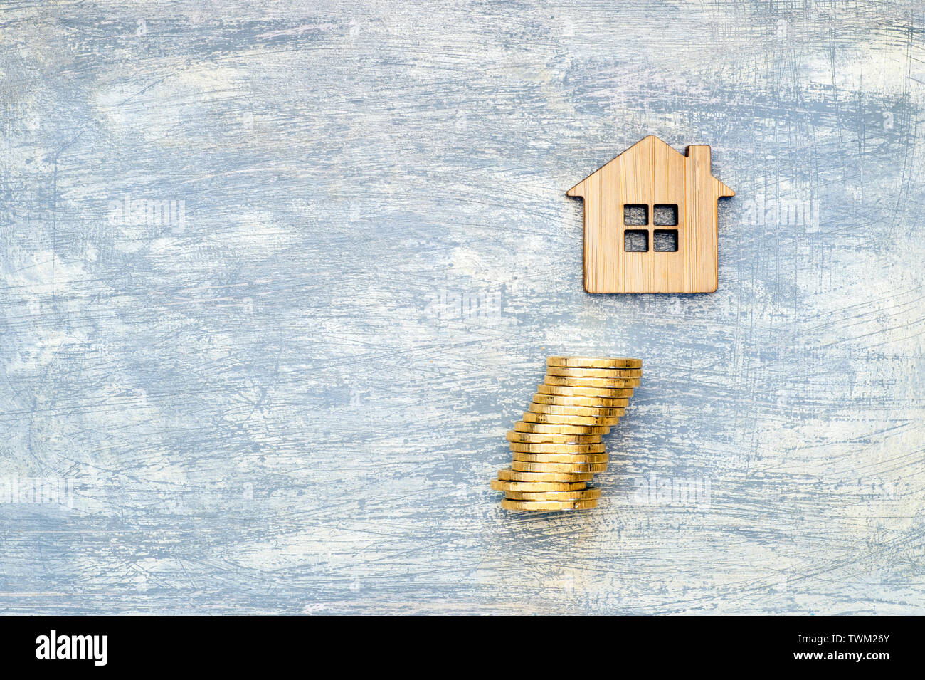 The house symbol is made of bamboo and yellow shiny coins on a scratched gray background with a blue tint. The concept of the offer of purchase of rea Stock Photo