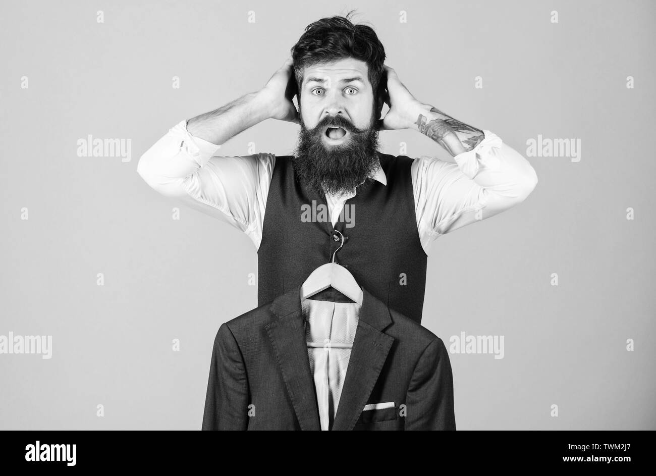 His wardrobe may shock you. Wardrobe assistant in shock with formal style coat. Shocked hipster at mens wardrobe. Bearded man choosing suit jacket at Stock Photo