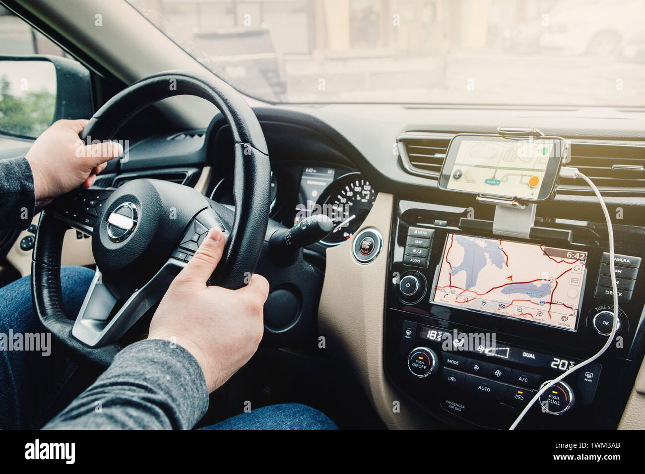 Closeup of man hands holding steering wheel. Person sitting in car using smartphone and build-in satellite navigator GPS. Modern gadgets in real life Stock Photo