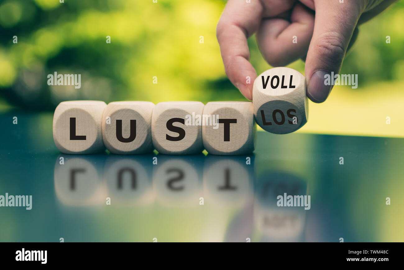 Hand turns a cube and changes the German word 'lustlos' ('listless' in English) to 'lustvoll' ('full of relish' in English). Stock Photo