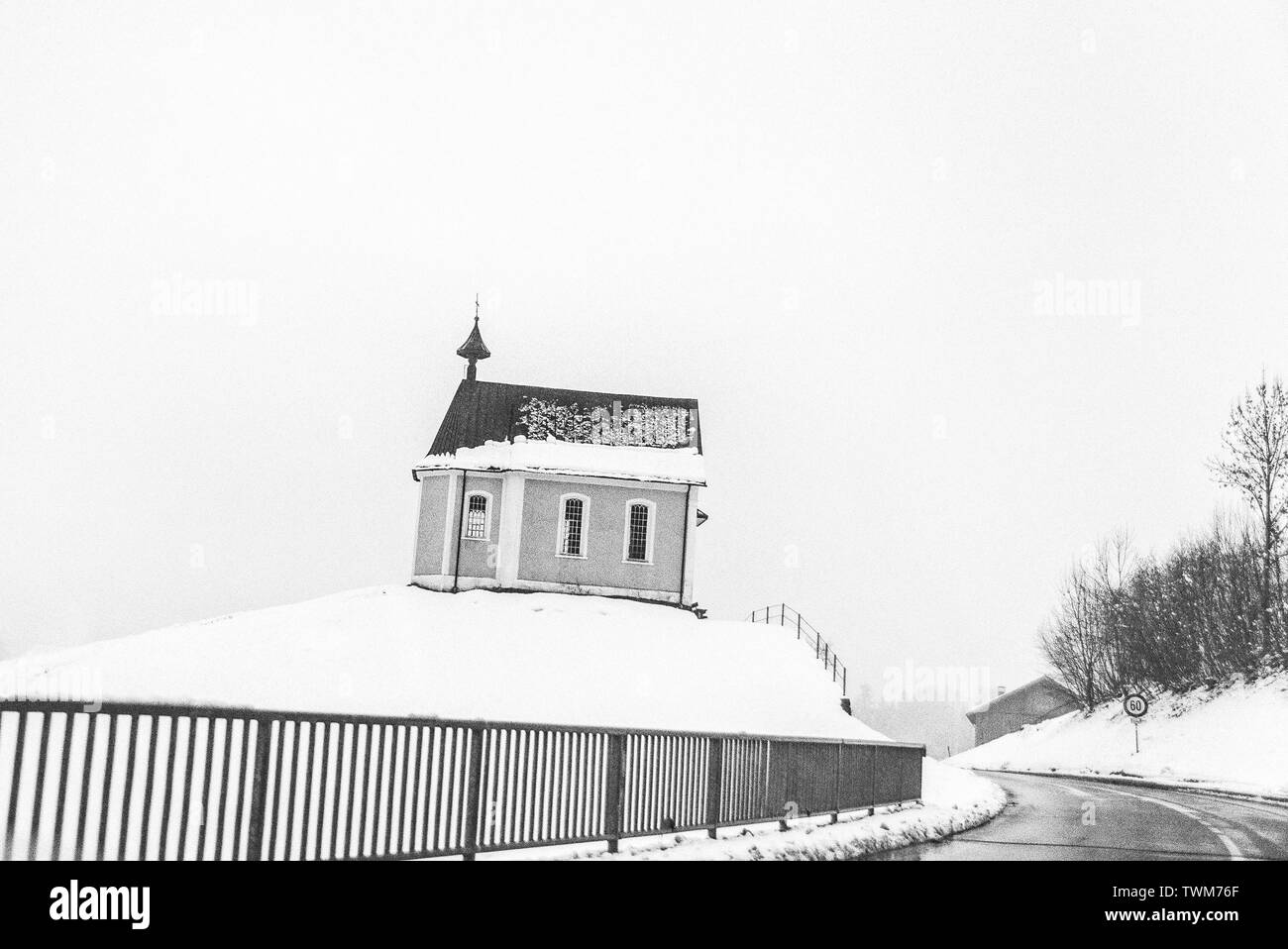 A small cottage almost covered with snow in the February 2011 winter is standing at the corner of a winding road leading to Egg, a village in Austria. Stock Photo
