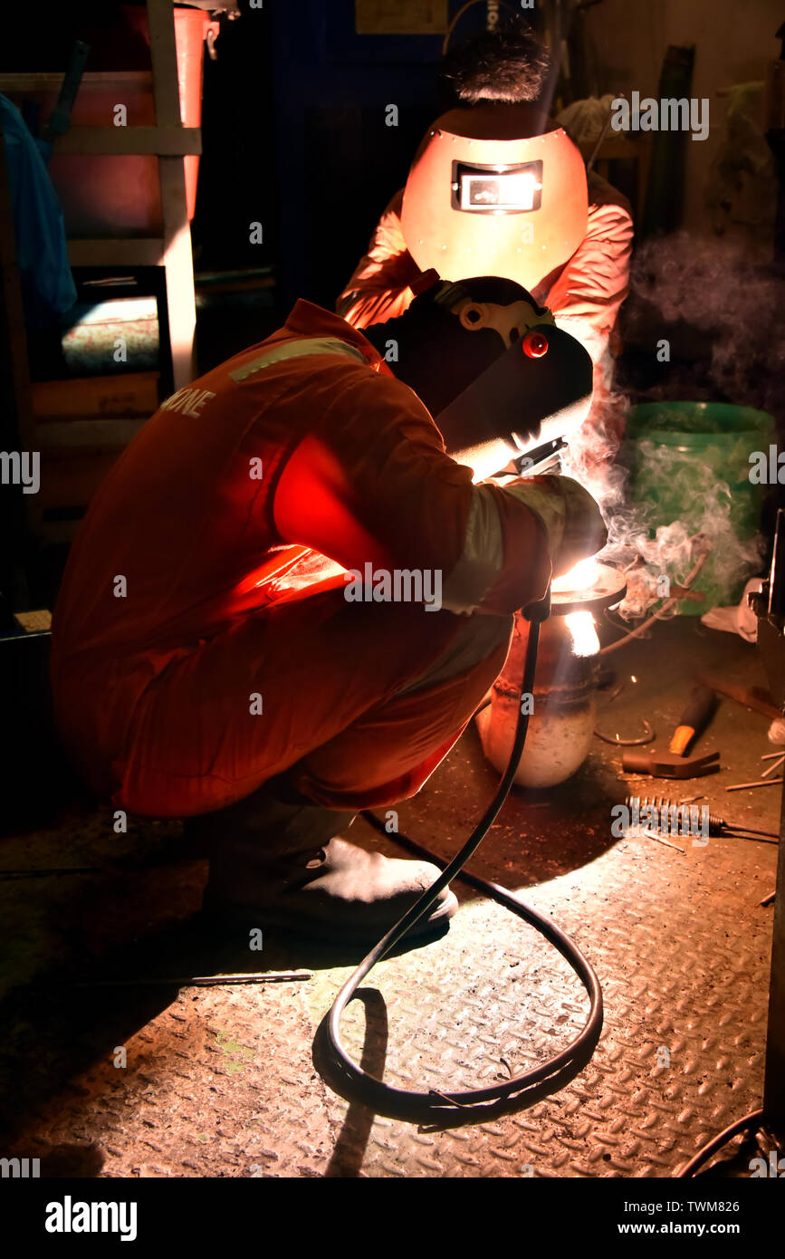welder and his helper fabricate pipe in a workshop wearing with complete personal protective equipment Stock Photo