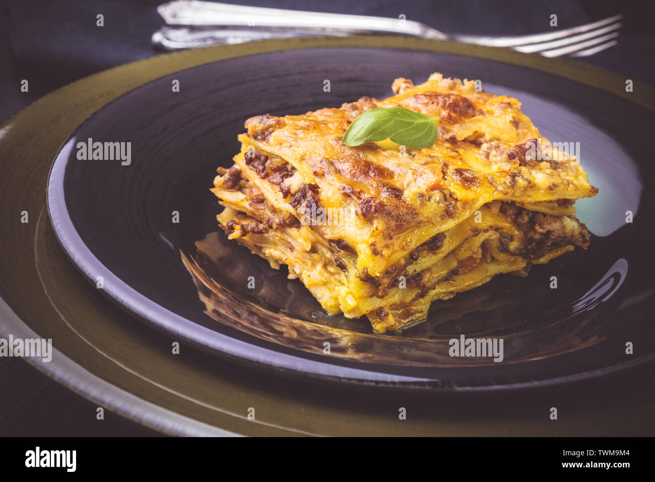Traditional Italian Lasagne with Minced Beef and Green Basil on Dark Plate Stock Photo