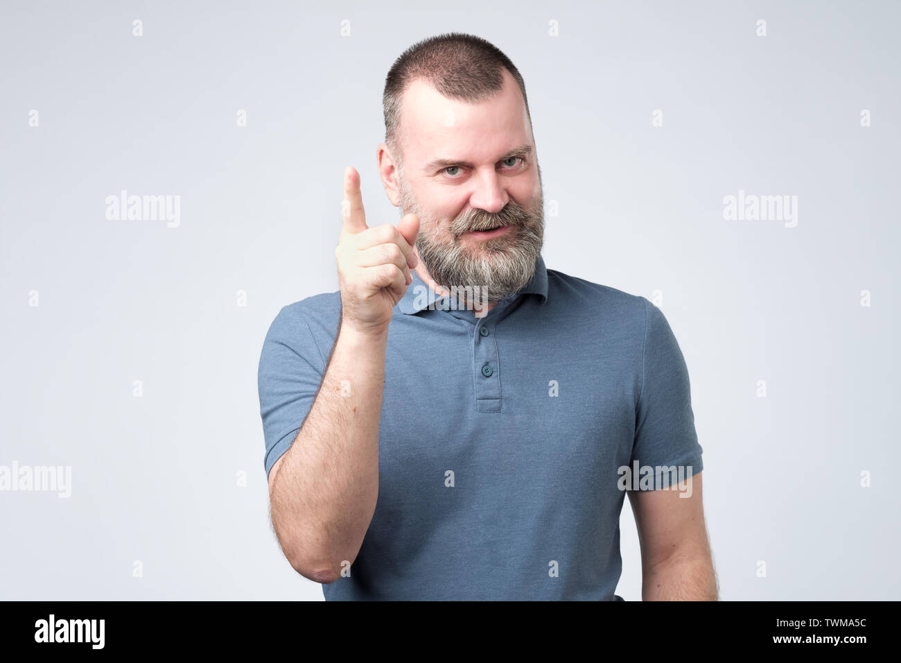 Satisfied mature man in blue clothes showing index finger up Stock Photo