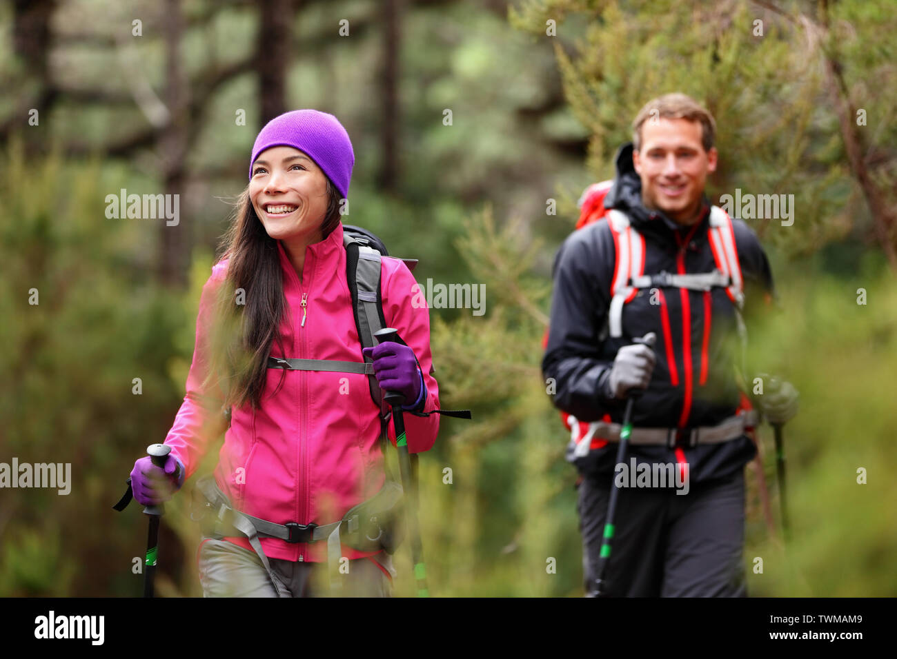 Hiking people - hikers trekking in forest on hike. Couple on adventure trek in beautiful forest nature. Multicultural Asian woman and Caucasian man living healthy active lifestyle in woods. Stock Photo