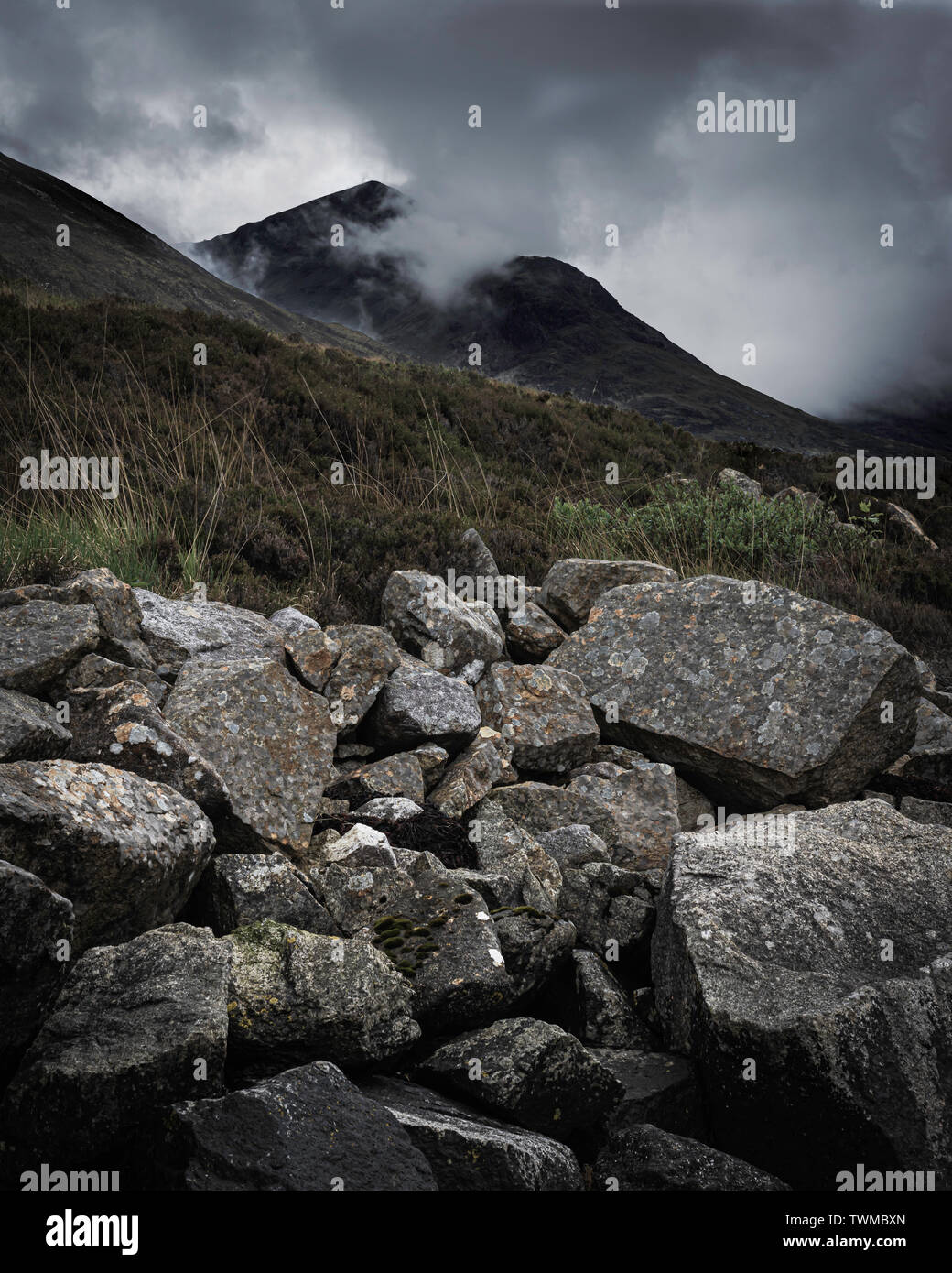 Clouds rolling over mountain peak and rocks in foreground.Dramatic landscape of Isle of Skye,Scotland.Dark nature image with atmospheric mood. Stock Photo