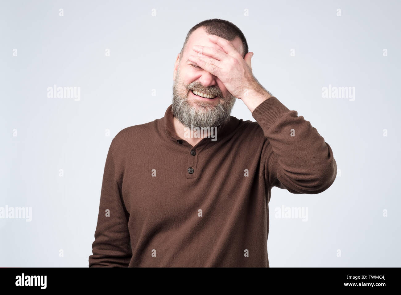 Mature handsome man wearing brown clothes smiling and laughing with hand on face covering eyes Stock Photo