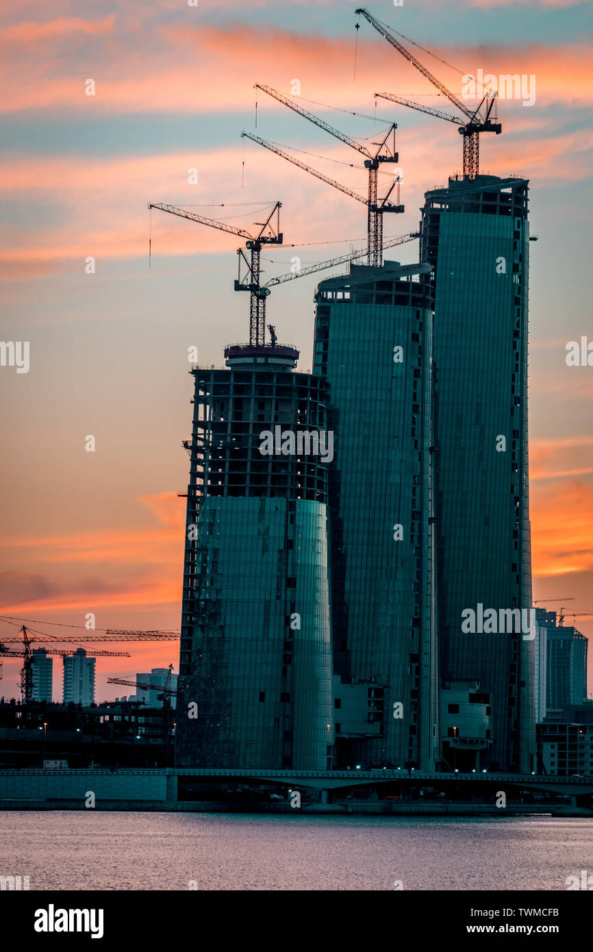 Bahrain skyline from Bahrain bay of three buildings during sunset with the ocean, three buildings still in construction Stock Photo