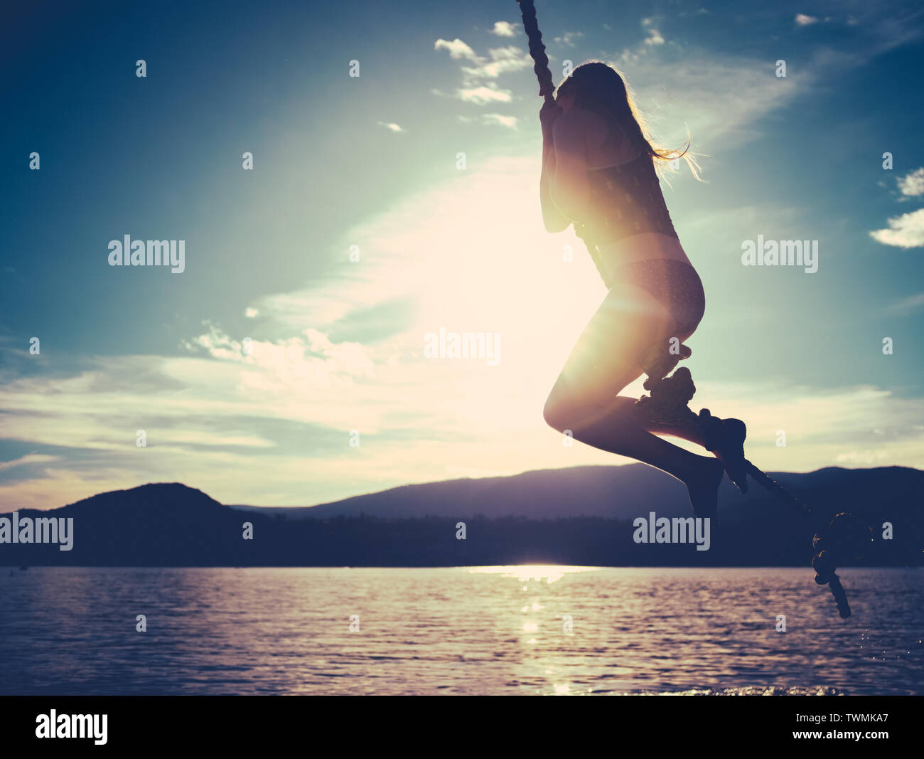 Retro Style Summertime Image Of A Girl Swinging Into A Lake At Sunset With Copy Space Stock Photo