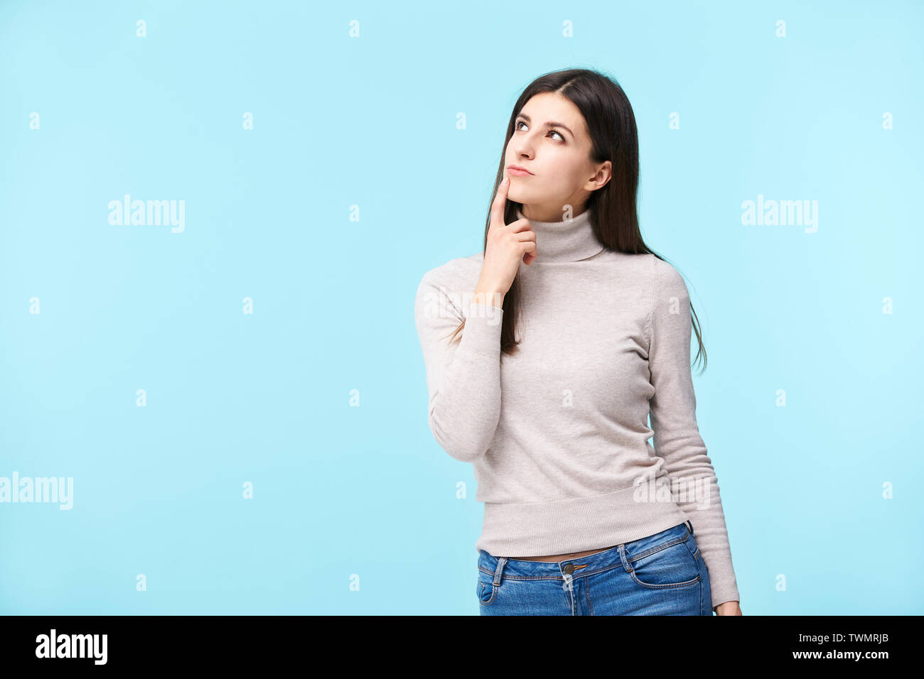 studio portrait of a beautful caucasian woman, looking up thinking, finger on lip, isolated on blue background Stock Photo