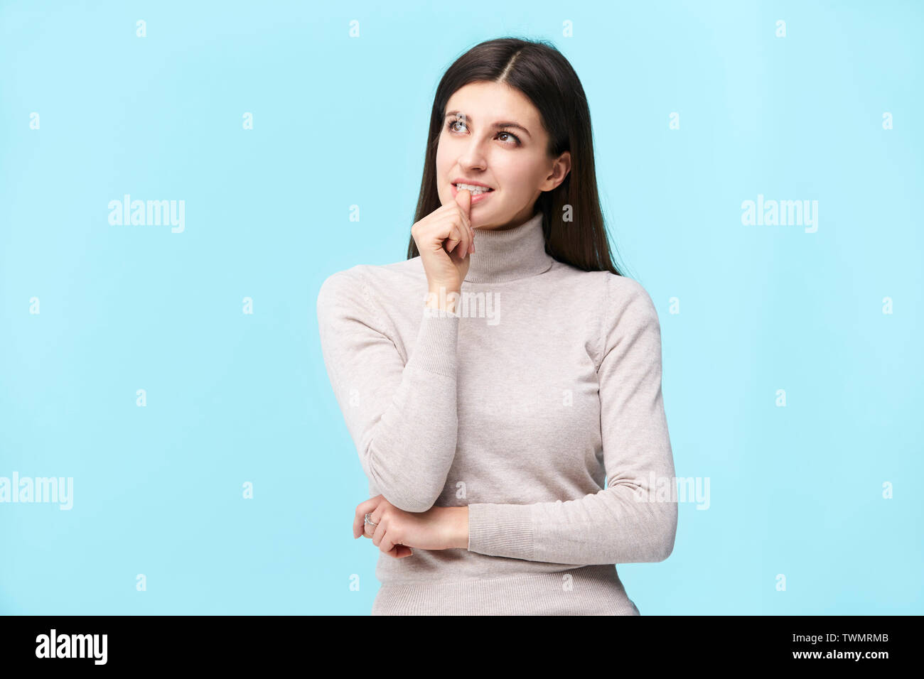 studio portrait of a beautful caucasian woman, looking up thinking, finger on lip, isolated on blue background Stock Photo