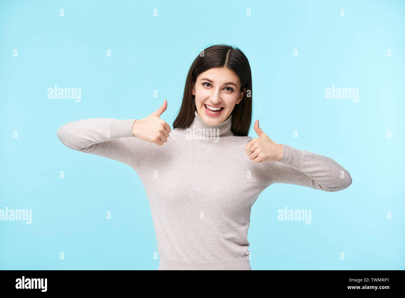 portrait of a beautiful young caucasian woman with two thumbs up, looking at camera smiling, isolated on blue background Stock Photo
