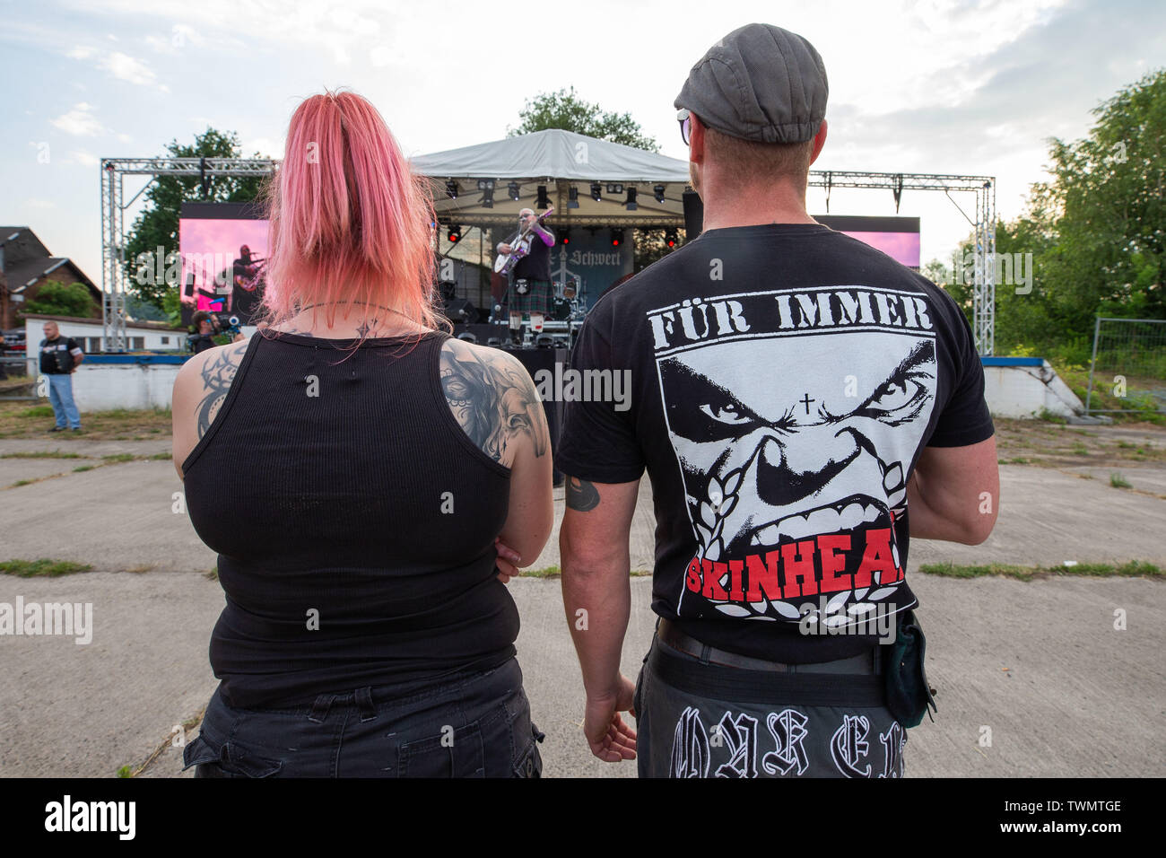Ostritz, Germany. 21st June, 2019. A man and a woman are standing on the area of the Schild und Schwert Festival in some distance to a stage. The man is wearing a T-shirt with the inscription 'FÜR IMMER SKINHEAD'. With the 4th Ostritz Peace Festival, the city of Ostritz wants to react to a new meeting of neo-Nazis to the Shield and Sword Festival in the East Saxon city. Credit: Daniel Schäfer/dpa-Zentralbild/dpa/Alamy Live News Stock Photo