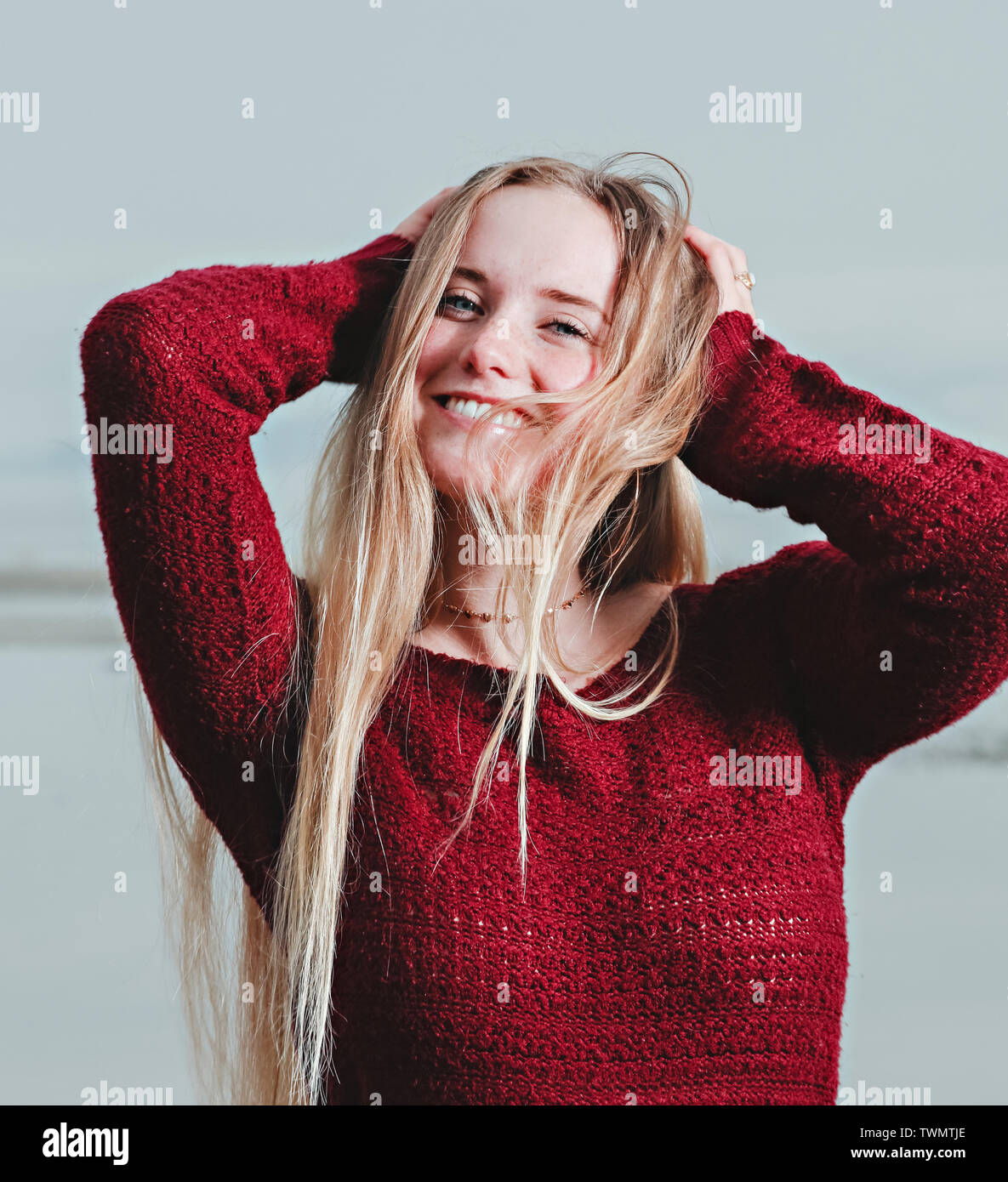 A young woman in a red shirt puts her hands through her long blond hair. Stock Photo