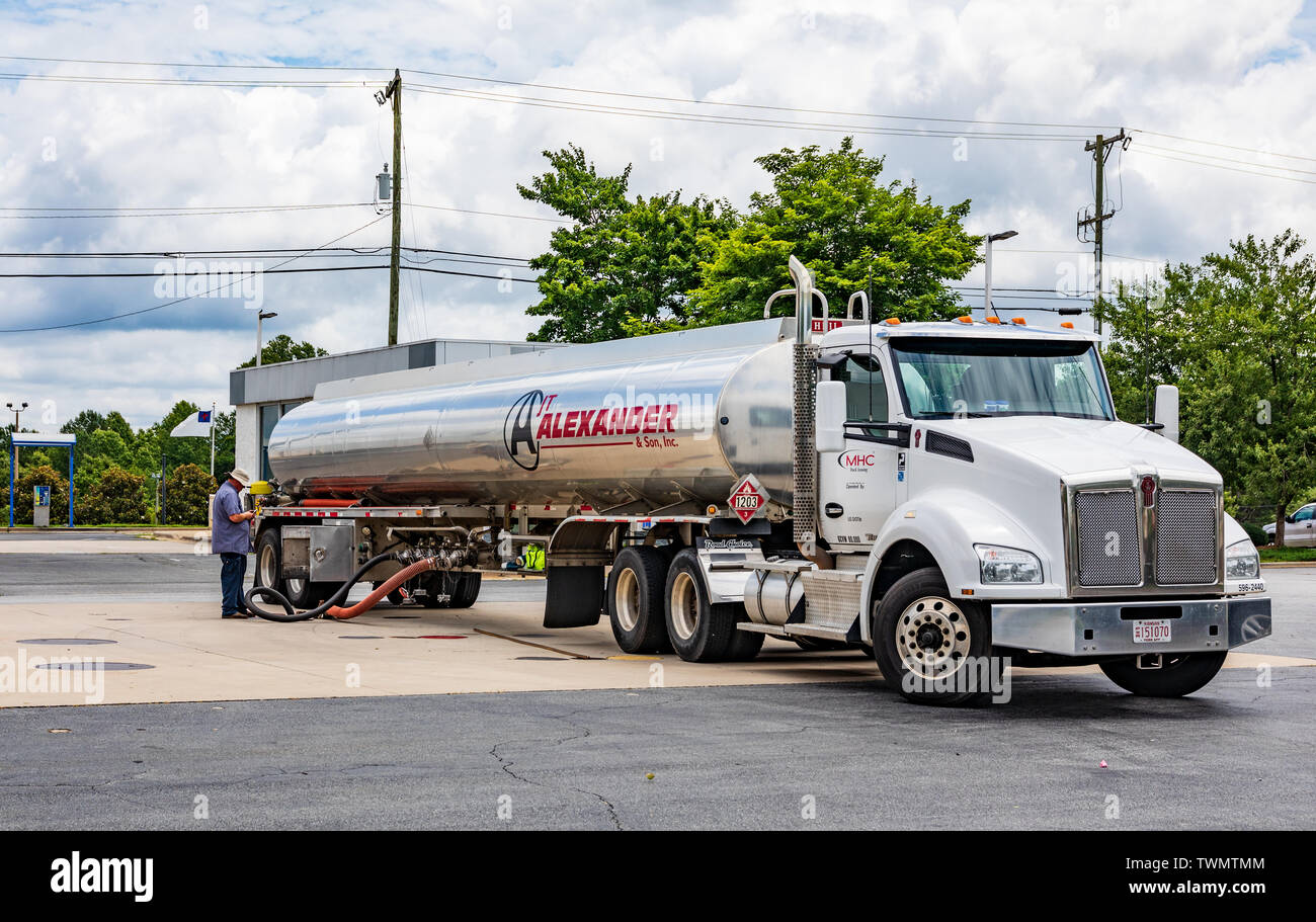 MOORESVILLE, NC, USA-JUNE 19, 2019:  An Alexander & Son tanker truck, filling a gas station tank, while driver stands by, looking at smart phone. Stock Photo