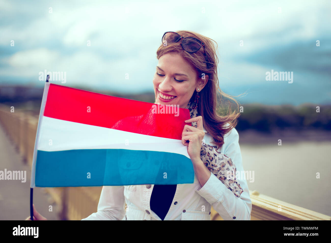 Happy young woman watching and holding Dutch flag, outdoors Stock Photo
