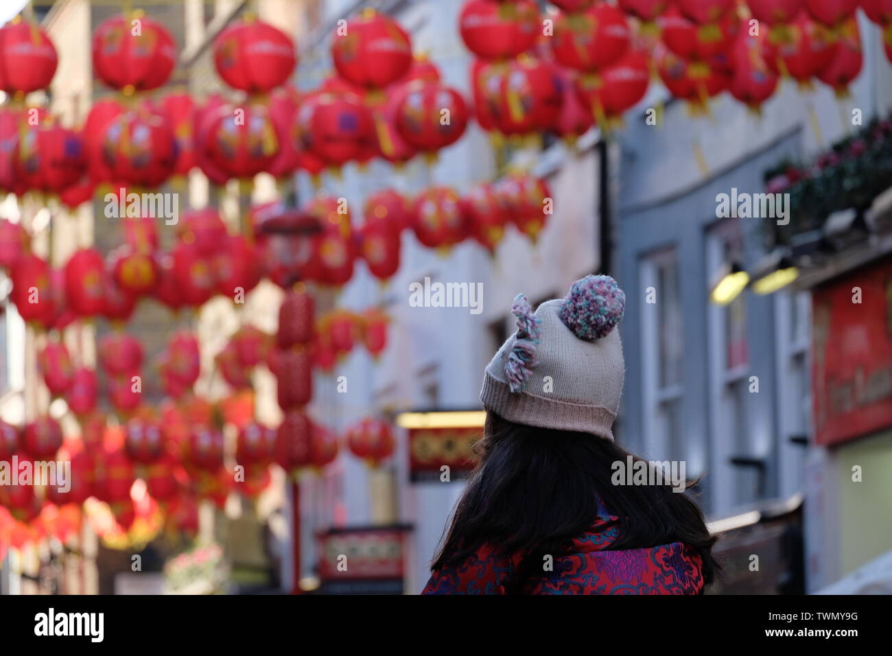 Asian girl wearing bobble hat sits on her parent's shoulders with Chinese New Year lanterns in background. Stock Photo
