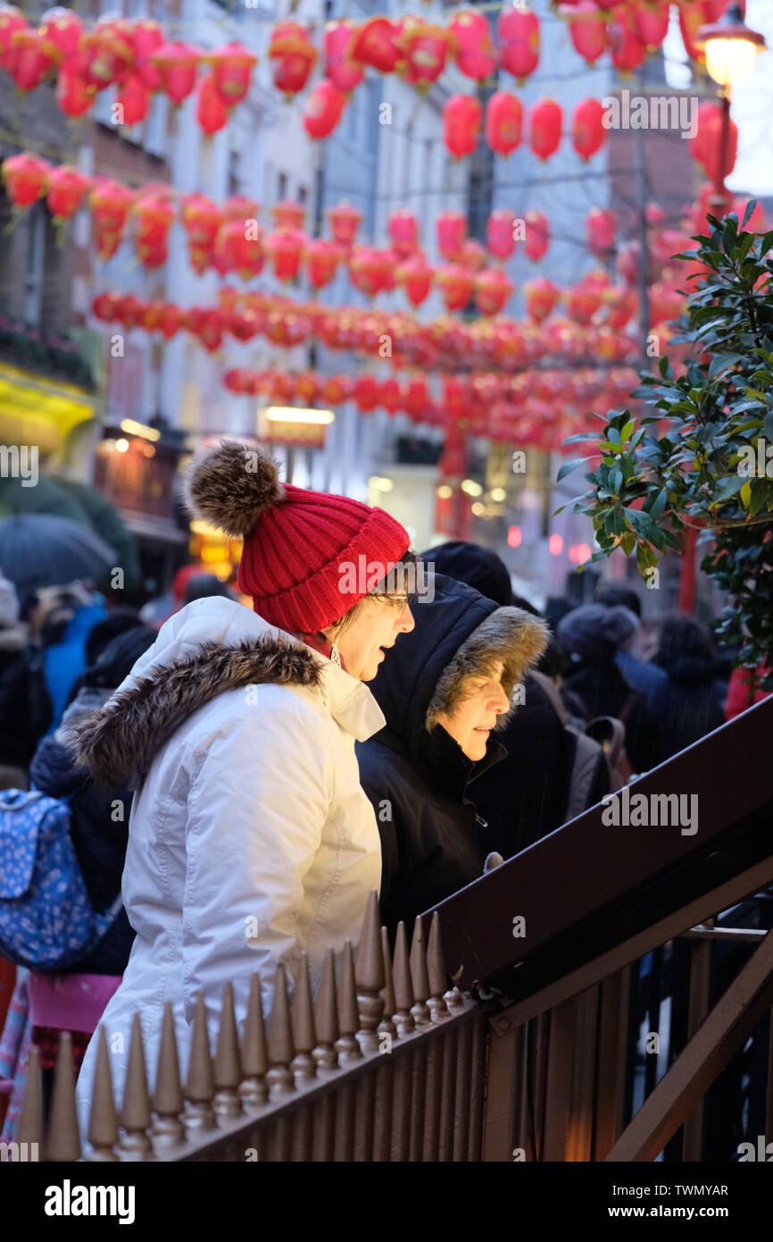 Two female diners in winterwear peruse a restaurant menu in London's Chinatown with Chinese lanterns in the background Stock Photo
