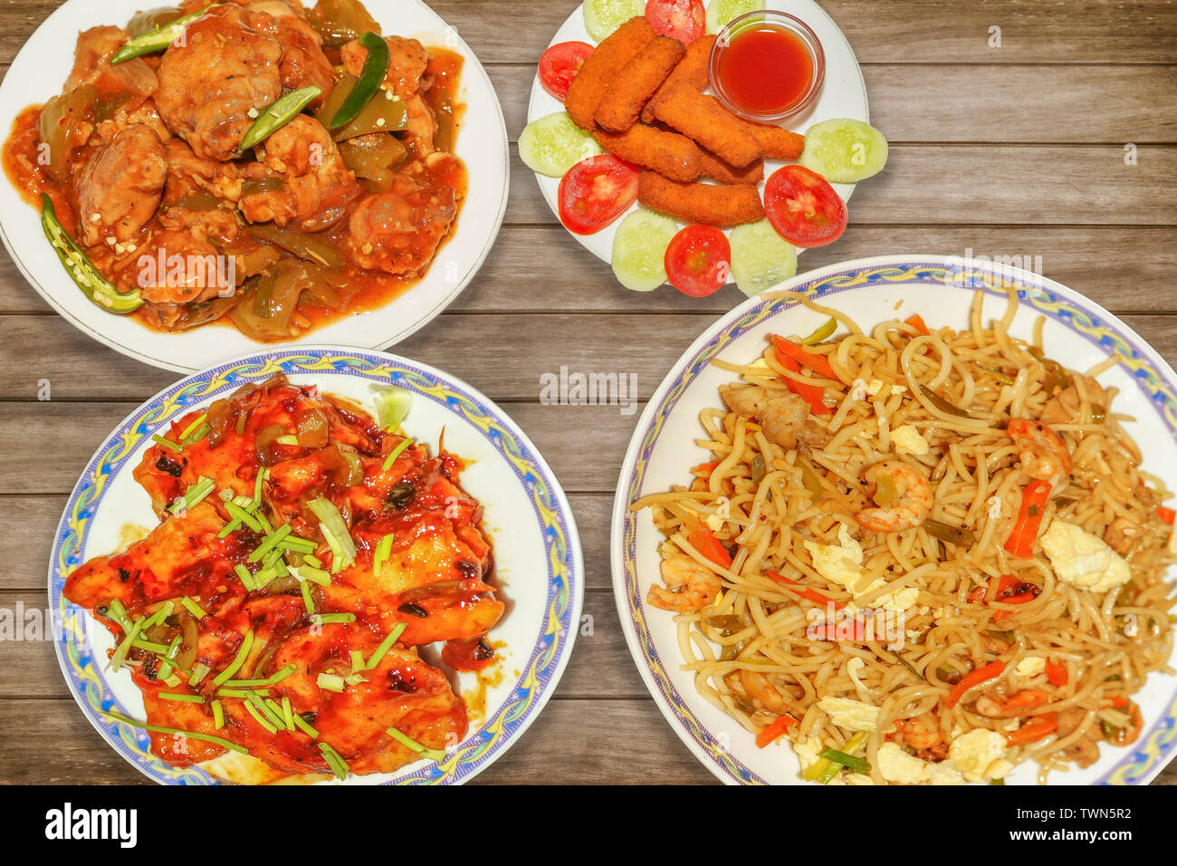 Indian food meal of spicy chicken chowmein with chilli chicken and red hot chilli fish along with crispy fish fingers served on wooden table Stock Photo