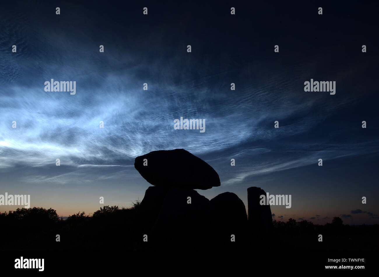 Night landscape with steel blue noctiliucent clouds with the silhouette of a round barrow in foreground. Stock Photo