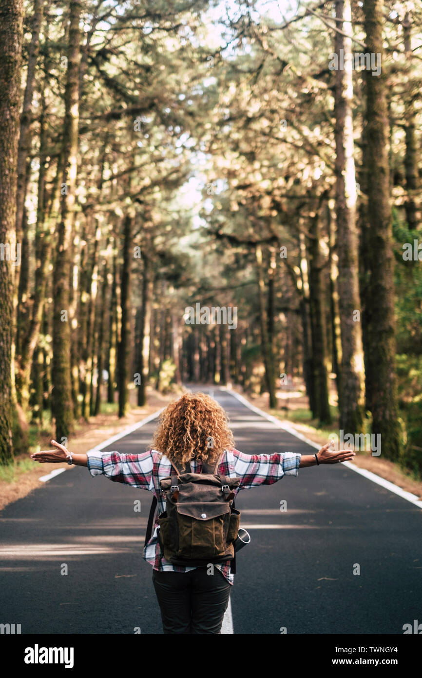 Alternative travel concept with curly hipster woman viewed from back open his arms and feel the freedom of the outdoors nature standing in the middle Stock Photo