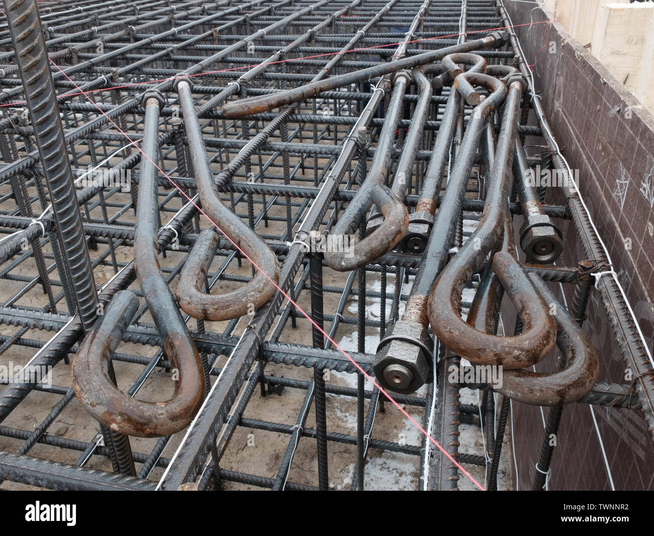 Steel anchor bolts with screw nuts laying on the steel grid of tower crane footing reinforcement. Stock Photo
