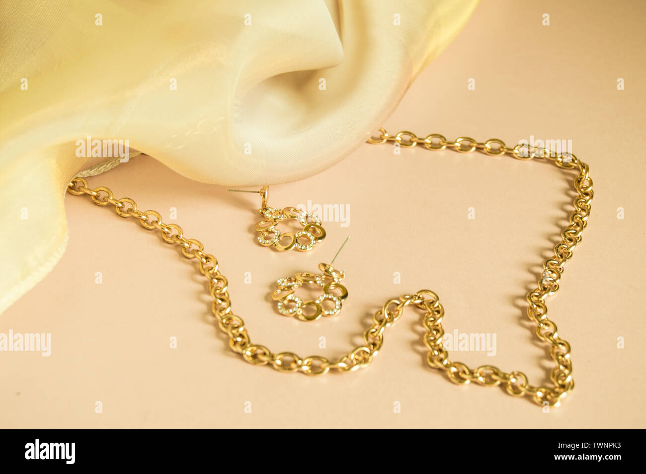 Luxury gold jewelry chain and earrings on pink background with silk, copy  space, selective focus Stock Photo - Alamy