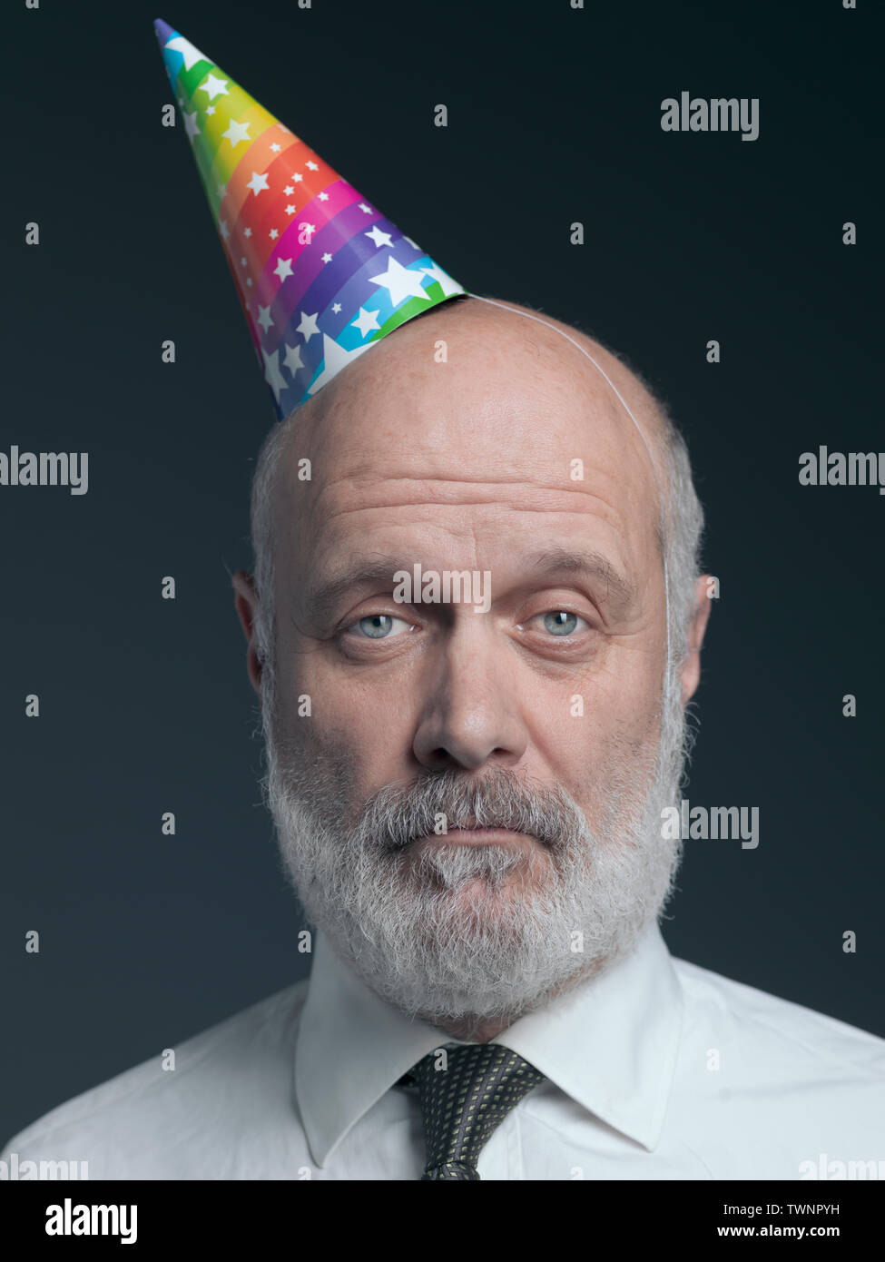 Funny senior bald man wearing a colorful party hat he is lonely, sad and disappointed Stock