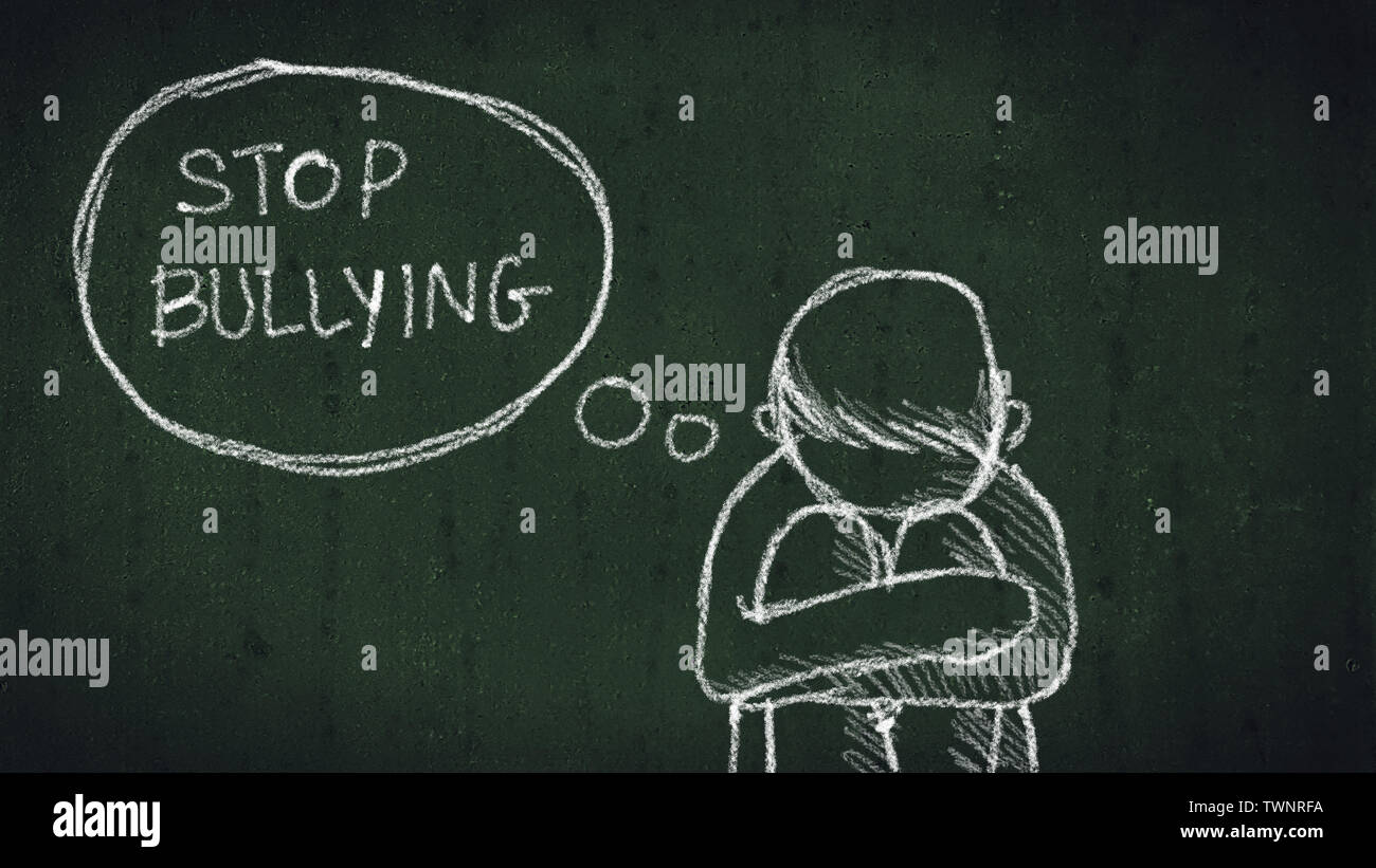 sad young boy sitting on the floor with text stop bullying written with chalk on chalkboard. social problems of humanity Stock Photo