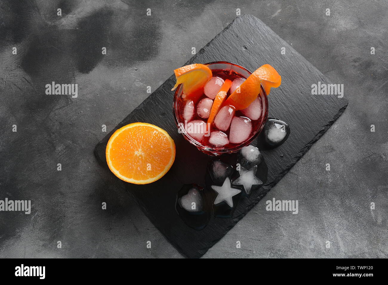 Negroni cocktail. Smoky Italian aperitif with gin, campari, martini Rosso, orange and ice cubes served in glass on dark stone background Stock Photo