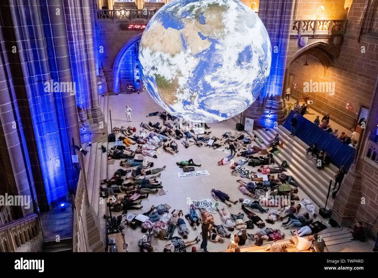 Liverpool, UK. June 22, 2019. Protesters from climate change group, Extinction Rebellion, hold a ‘die-in’ protest at Liverpool’s Anglican Cathedral underneath Gaia, an art installation consisting of a 23ft replica of the Earth. Protesters laid down under the installation for 25 minutes which aimed to highlight lack of action on climate change. Credit: Christopher Middleton/Alamy Live News Stock Photo