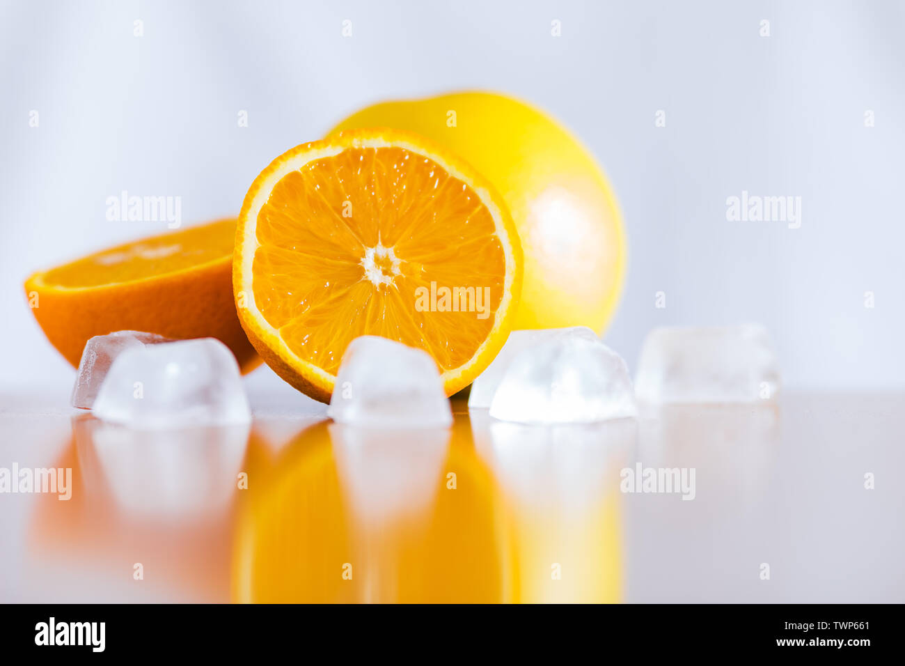 Fresh oranges and ice cubes on reflective wooden table Stock Photo