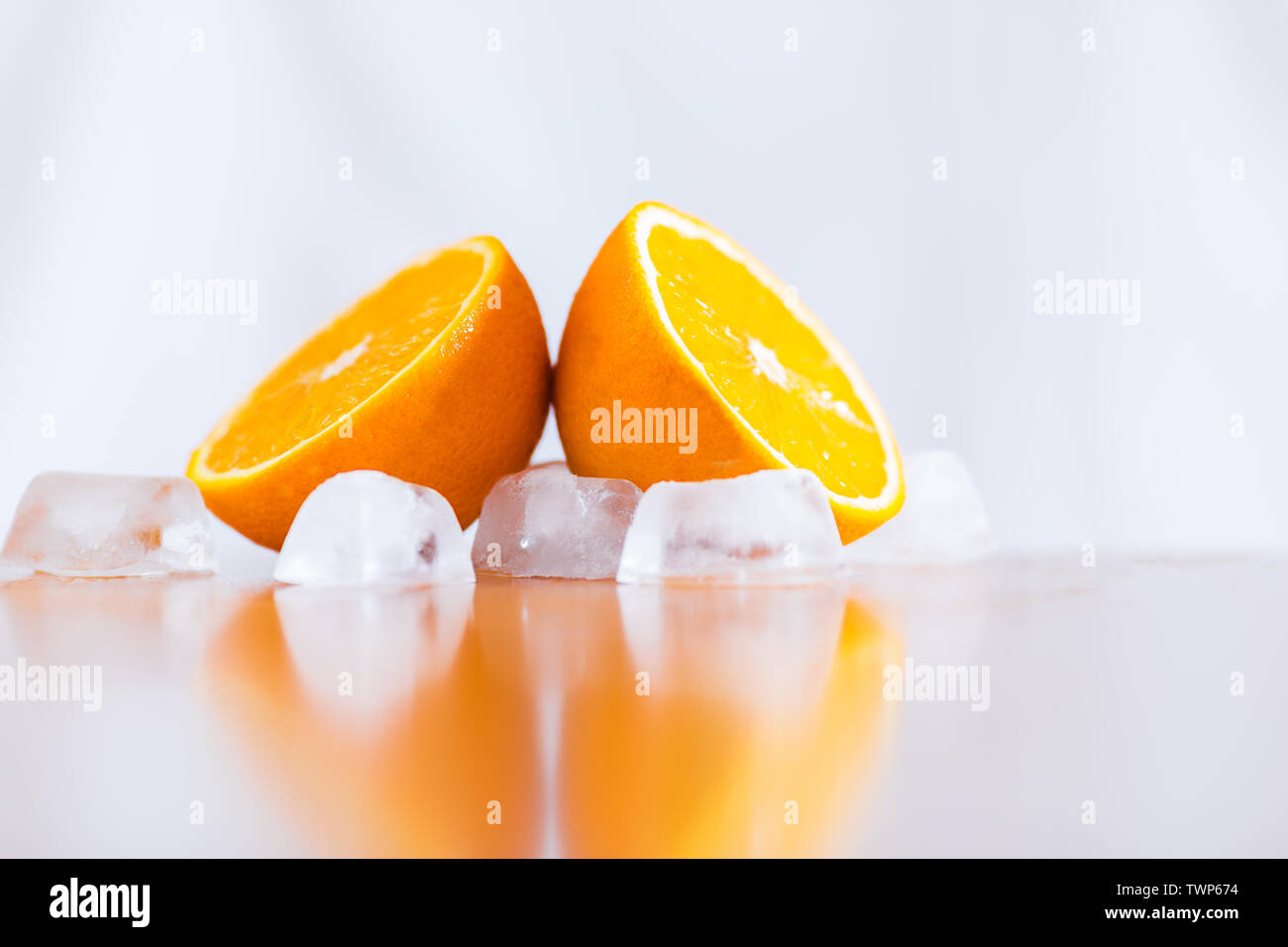 Fresh oranges and ice cubes on reflective wooden table Stock Photo