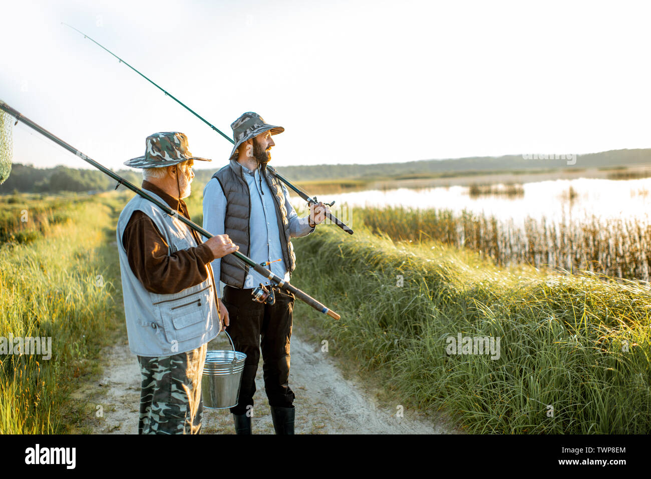 https://c8.alamy.com/comp/TWP8EM/grandfather-with-adult-son-walking-with-fishing-gear-on-the-footpath-near-the-lake-during-the-morning-light-TWP8EM.jpg