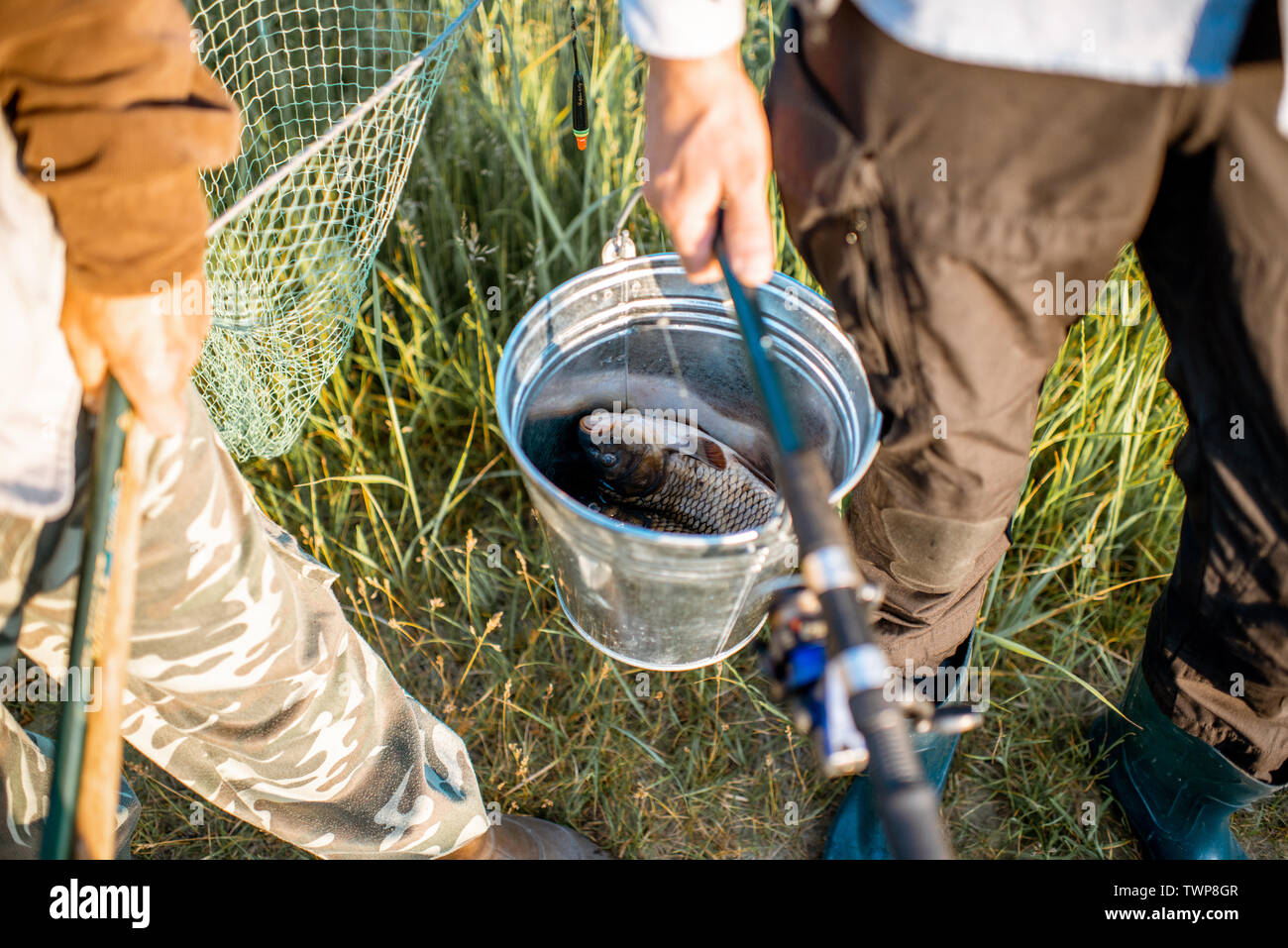Men holding fishing rods and bucket with fresh caught fish outdoors. Close-up  view with no face Stock Photo - Alamy